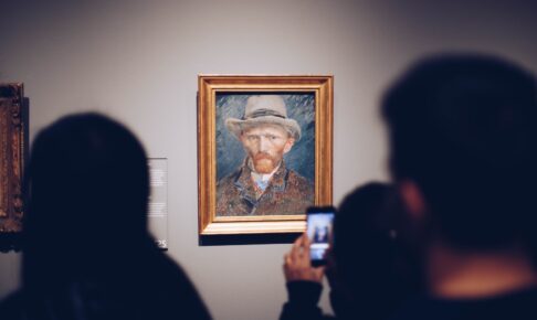person taking picture of man wearing brown hat painting