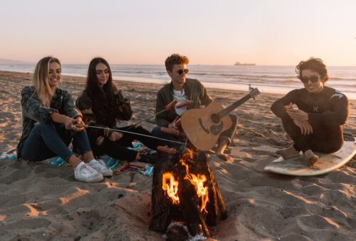 people sitting on sand near bonfire during daytime