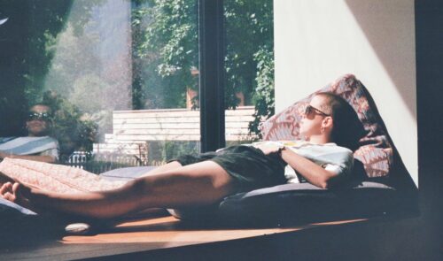 man lying on cushion beside glass window