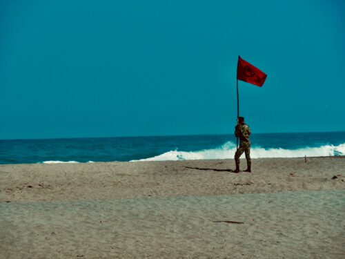 woman in black and white dress holding red flag standing on beach during daytime