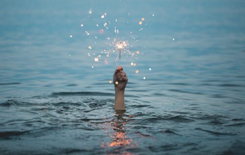 person submerged on body of water holding sparkler