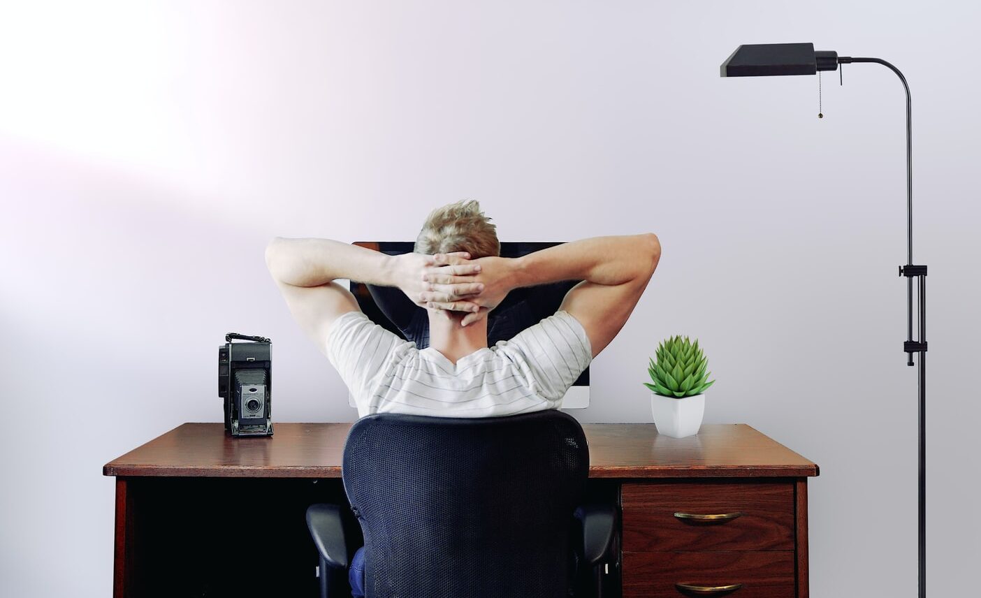 man holding his head while sitting on chair near computer desk