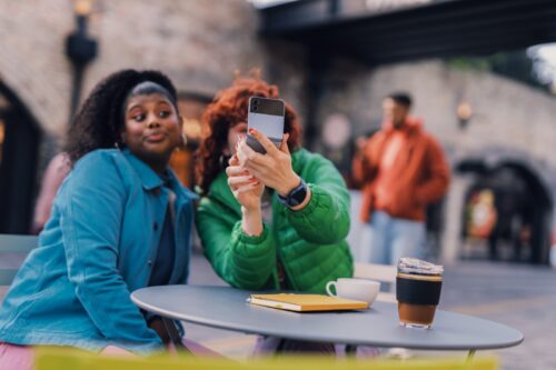 a couple of women sitting at a table with a drink and a cell phone