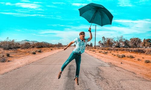 woman in teal long sleeve shirt and blue denim jeans holding umbrella walking on road during