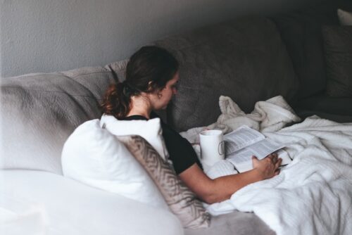 woman reading book sitting on gray sofa