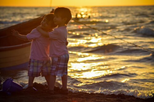 two boys standing on seashore during sunset