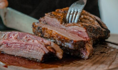 person slicing a meat on brown wooden board