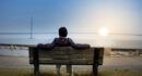 person sitting on bench facing suspension bridge