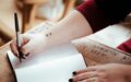 person holding pen above white open notebook page