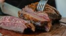 person slicing a meat on brown wooden board